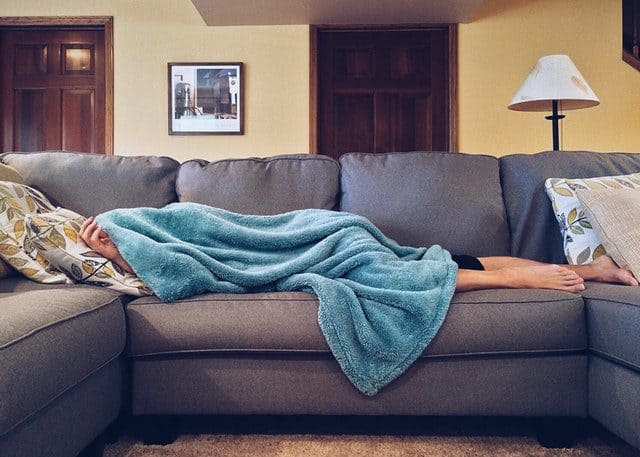 Een vrouw ligt ontspannen op een bank, gewikkeld in een zachte, turquoise deken, terwijl ze zich comfortabel maakt in een gezellige woonkamer.