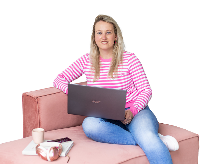 Een vrouw met lang blond haar zit op een roze bank en werkt op een laptop. Naast haar staan een kopje koffie en een smartphone, wat een gezellige werkplek suggereert.