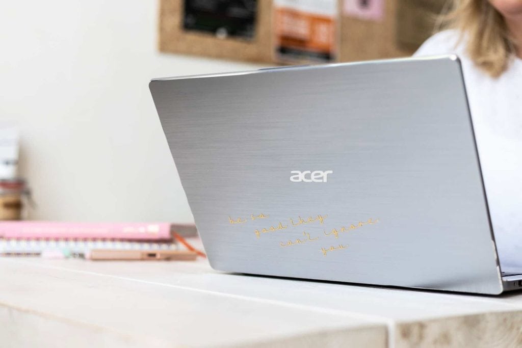 Acer laptop met een inspirerende boodschap op de achterkant, geplaatst op een bureau met notitieboeken en een georganiseerde achtergrond.