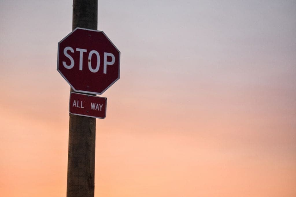 Stopbord met de tekst "ALL WAY" eronder, tegen een achtergrond van een kleurrijke zonsondergang.