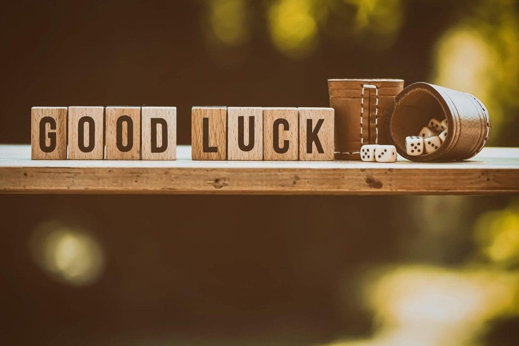 Houten blokken met de tekst "GOOD LUCK" staan op een houten tafel naast een omgevallen mand met dobbelstenen. De afbeelding straalt een positieve en speelse sfeer uit, perfect voor gelukwensen.