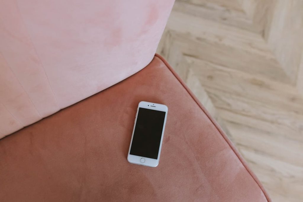 Een smartphone ligt op een zachte, roze bank, met een houten vloer op de achtergrond.