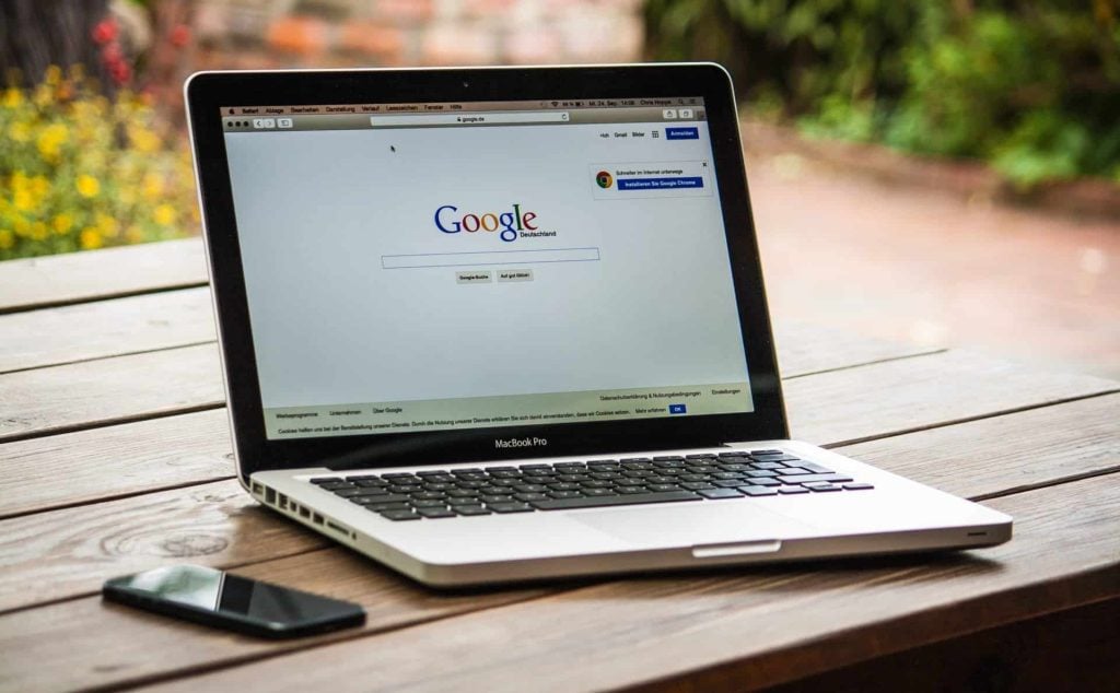 Laptop met het Google zoekscherm op een houten tafel, naast een smartphone. De afbeelding benadrukt het gebruik van technologie voor informatiezoektochten.