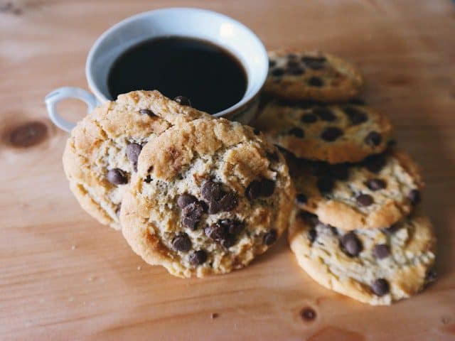 Vers gebakken chocolate chip cookies liggen naast een kopje zwarte koffie op een houten tafel. Perfect voor een gezellige pauze of dessertmoment.