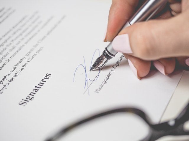 Een hand schrijft een handtekening met een vulpen op een document met de titel 'Handtekeningen'. Het beeld benadrukt het belang van officiële documenten en overeenkomsten.