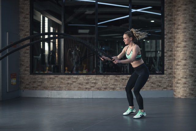 Vrouwelijke atleet die met een fitnesskoord traint in een moderne sportschool. De focus ligt op haar krachtige bewegingen en sportieve outfit.