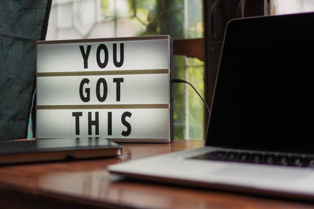 Verlichte tekstlamp met de boodschap "YOU GOT THIS", geplaatst op een houten bureau naast een laptop en een notitieboek. Deze inspirerende decoratie stimuleert motivatie en creativiteit in een werkruimte.