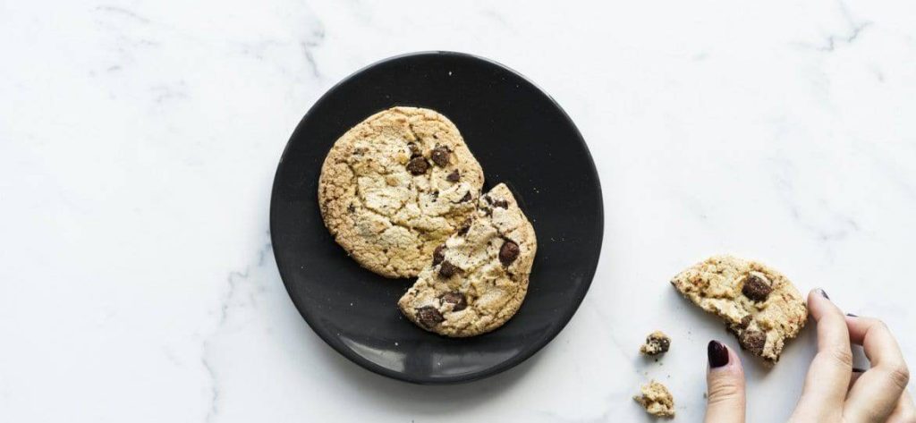 Verse chocoladekoekjes op een zwart bord, met een hand die een stuk van een koekje afbreekt. Perfect voor een zoete traktatie of dessert.